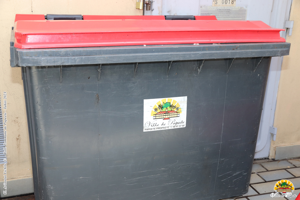 Une poubelle grise avec couvercle rouge et le logo de la Ville de Papeete